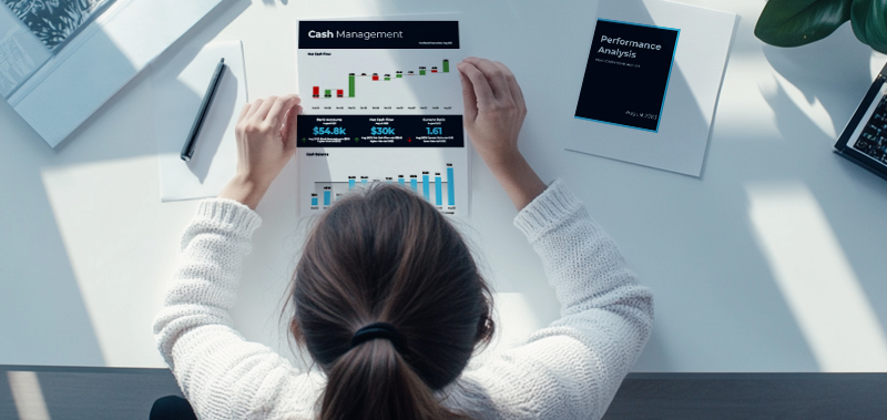 A professional woman sitting at a desk, carefully reviewing a cash flow report, with financial documents and charts displayed in a modern office setting.