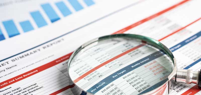 A magnifying glass placed over financial reports, symbolizing a detailed review of IFRS regulations and financial compliance.