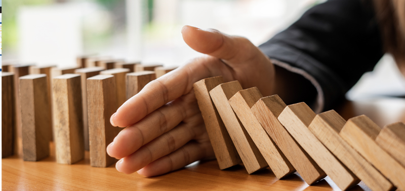 Hand stopping wood blocks from falling, representing risk management strategies to prevent financial losses.
